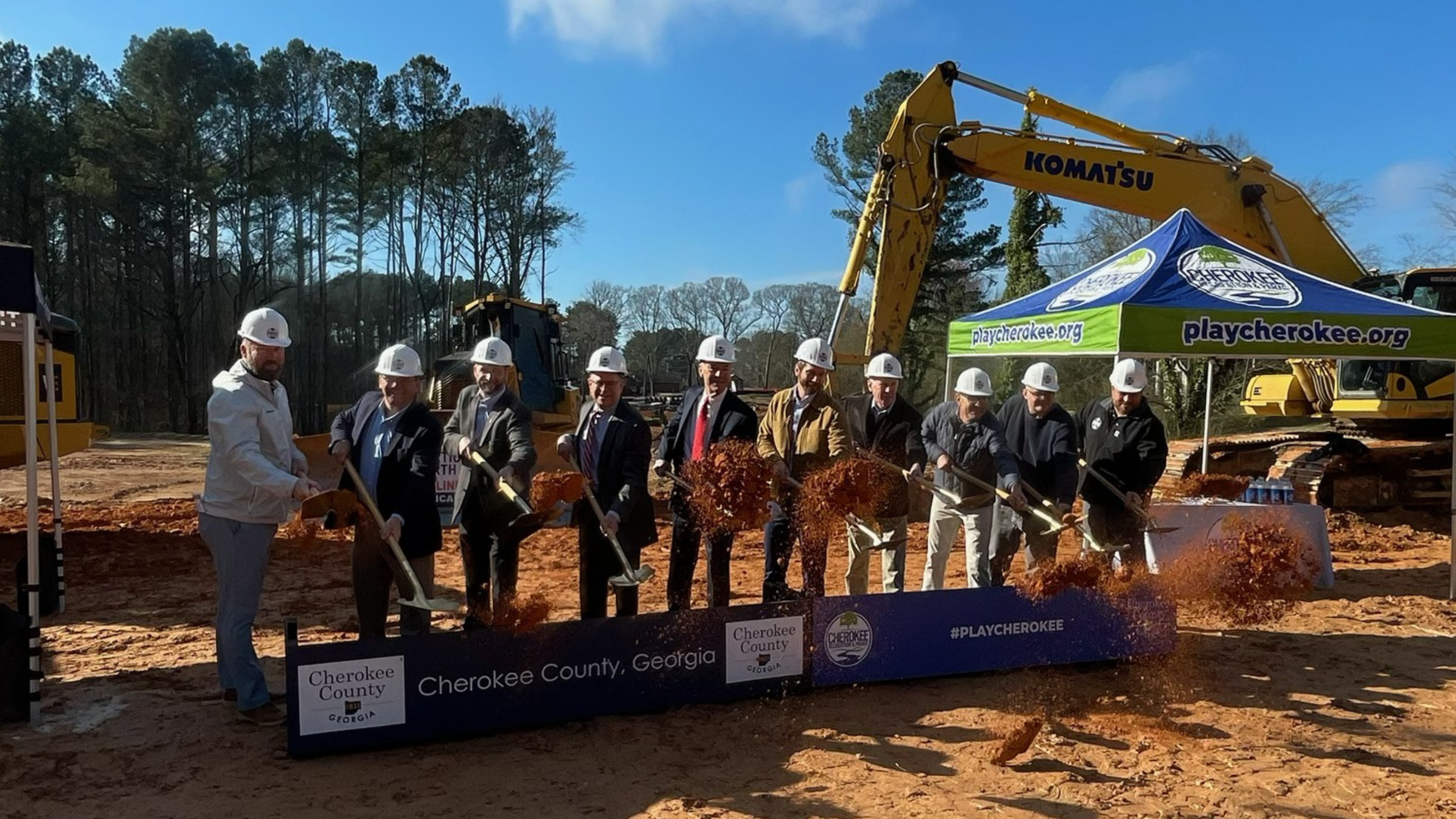 Image of 10+ people in hard hats posed shoveling dirt